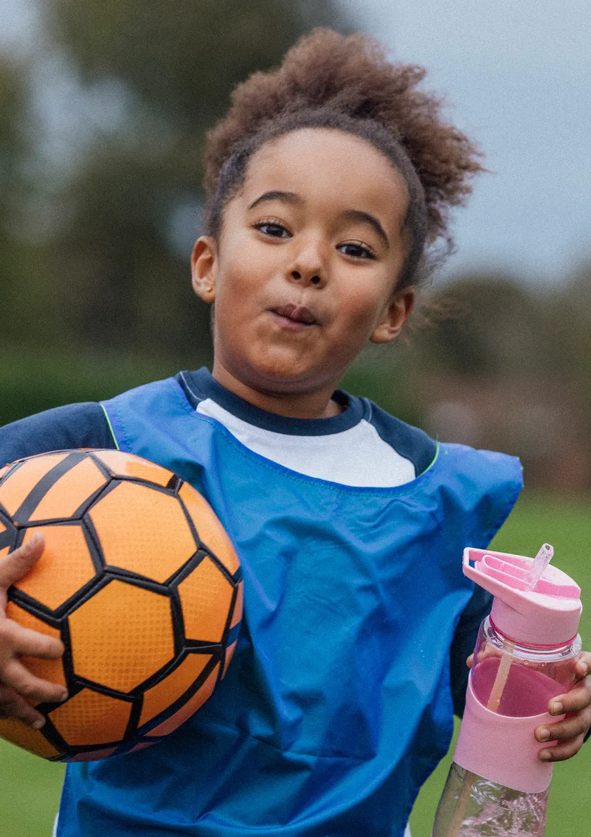 young girl looking happy holding football and her water bottle