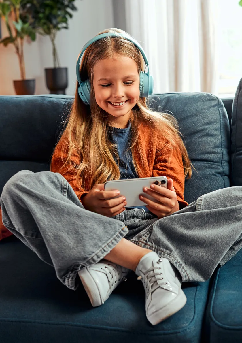 young girl sitting on the sofa with her headphones using mobile device